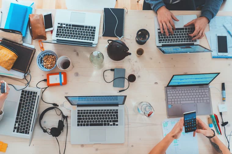 A desk seen from above, covered in laptops and notebooks