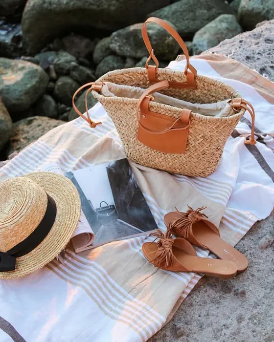A woven bag, a straw hat and leather sandals on a striped towel