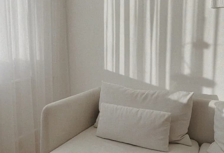 A pale sofa under a window, curtain shadows falling across the wall