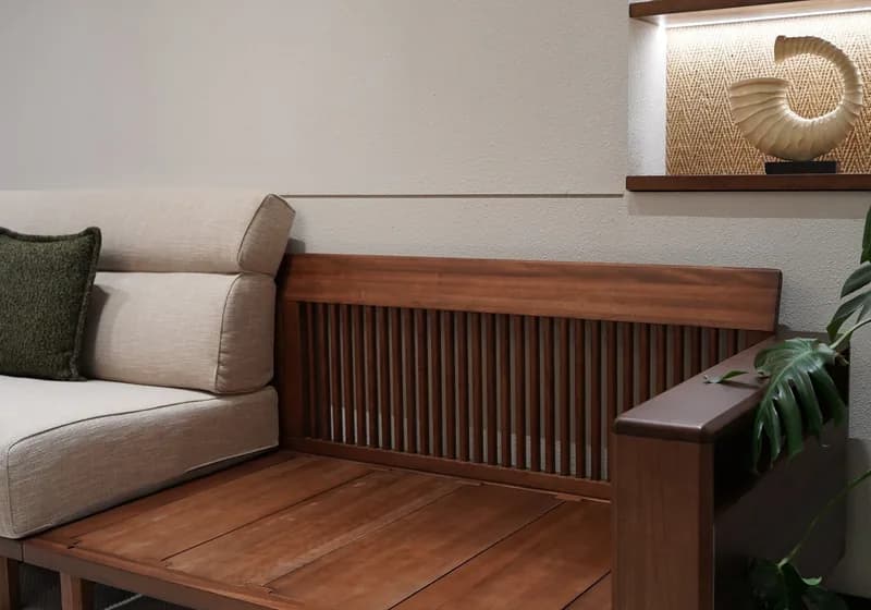 A slatted walnut bench seat with linen cushions against a pale wall