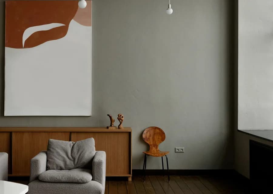 A quiet living room with an olive wall, a low walnut sideboard and a single armchair